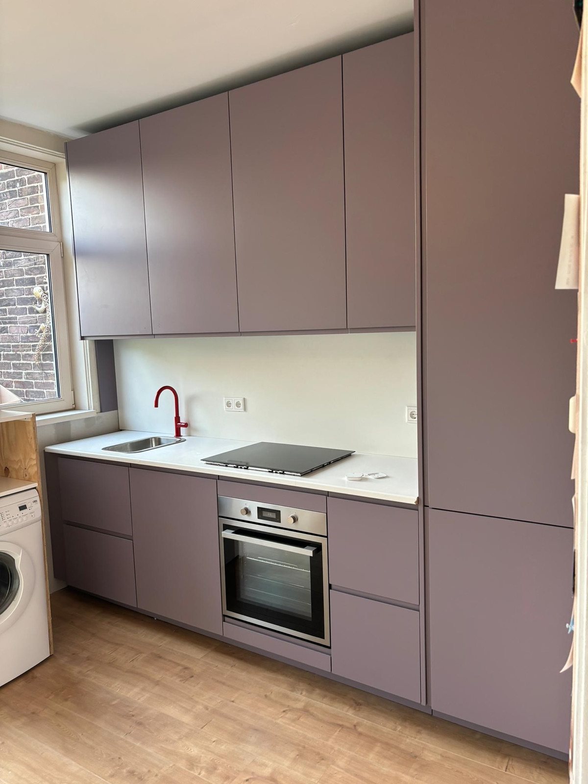 Afgewerkte keuken met paarse fronten, wit werkblad en rode kraan